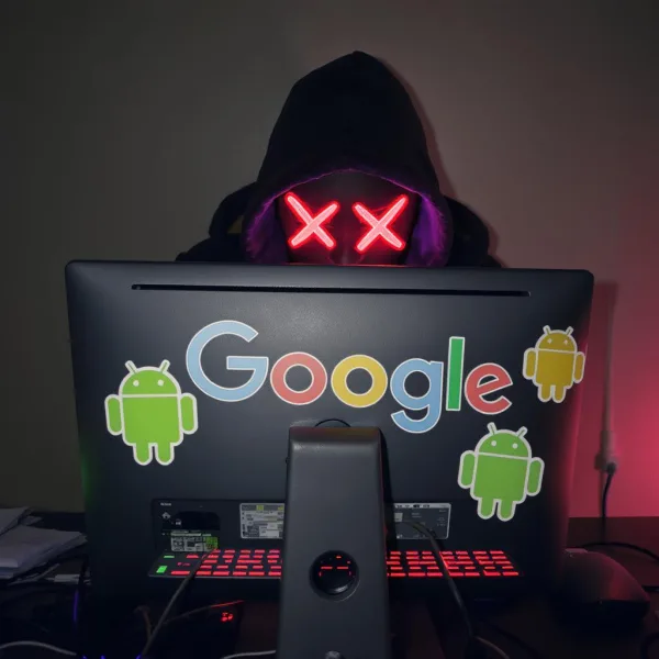 A hacker on a laptop with Google and Android stickers on it
